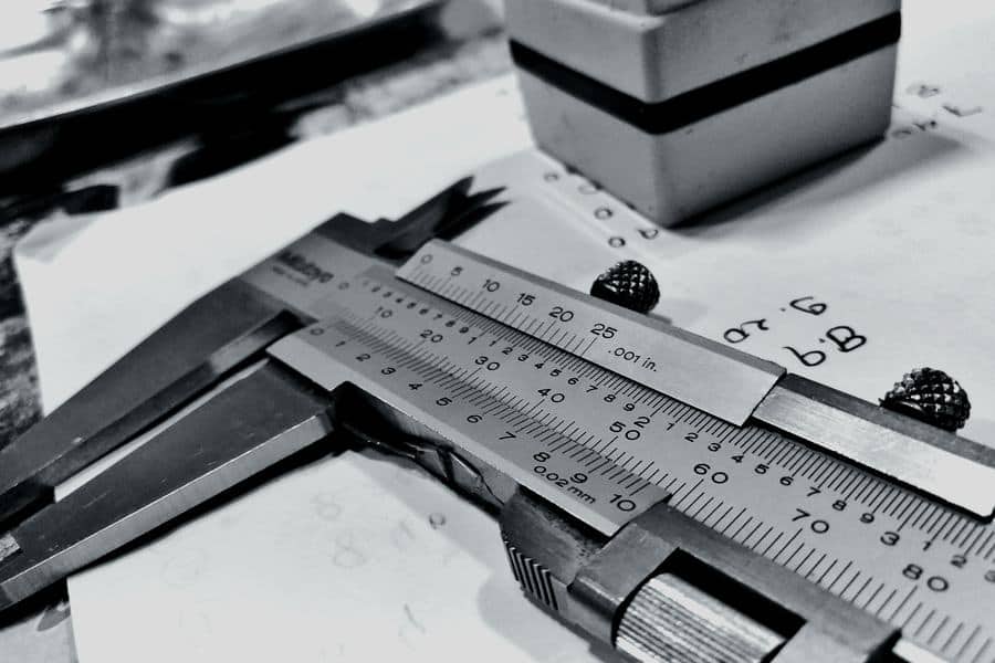 Teknik çizimin üzerinde duran sürmeli kumpas ve ölçülen metal parça.